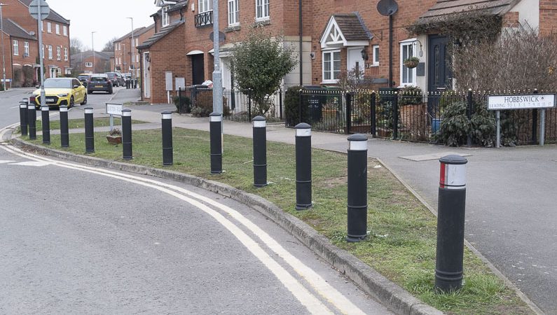 a number of bollards on a grass verge at a road junction